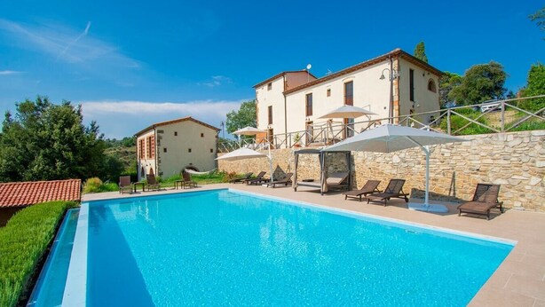 A rectangular swimming pool with lounge chairs and umbrellas, surrounded by stone walls and a building with a tiled roof. - Villa Gropia - Private Tuscan villa with pool (Palaia)