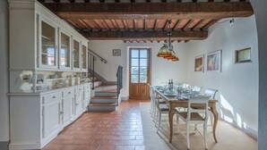 A spacious kitchen with a wooden staircase, a dining area with a table set for four, and a view of the outside through a window. - Villa Gropia - Private Tuscan villa with pool (Palaia)