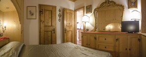A bedroom with a bed, wooden wardrobe, a television, and a mirror. - Villa Lucente  (Cortina d´Ampezzo)