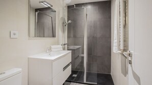 Ett modernt badrum med en duschavdelning med glasväggar, ett vitt handfat och en stor spegel.