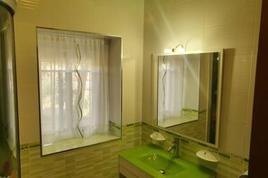 Un baño con un lavamanos verde, un espejo y una ventana con cortina.