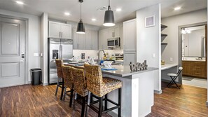 A modern kitchen with a central island, stainless steel appliances, and wicker bar stools. - DFW Elevator 2bd 2bth Ext Patio Zen Place futon couch I35 easy access elevators  (Fort Worth)