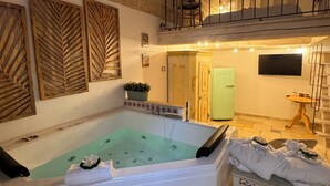 A spa area with a large bathtub, a balcony with a railing, and a television mounted on the wall.