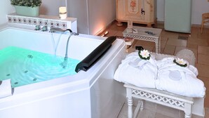 A bathtub with running water, a white towel with a flower, and a small table with a book and a candle.