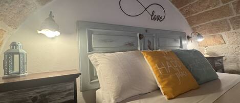 Quarto com cama, mesa de cabeceira, um candeeiro e uma parede com a inscrição 'love'.