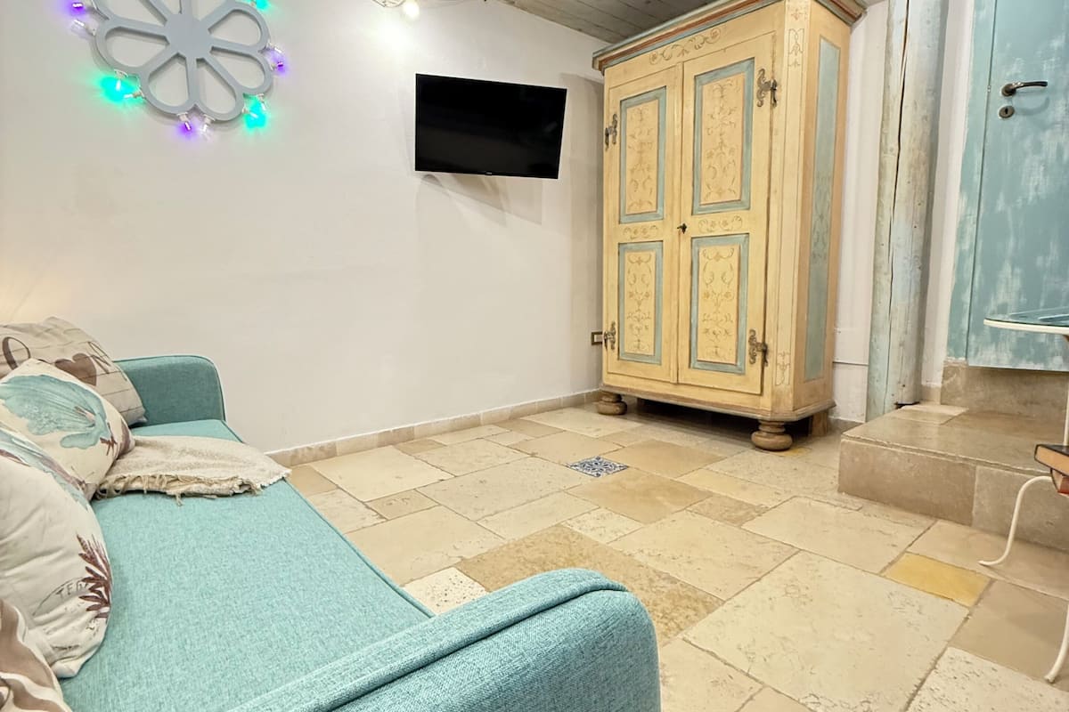Una habitación con sofá color turquesa, un mueble de madera, un televisor y una lámpara decorativa.