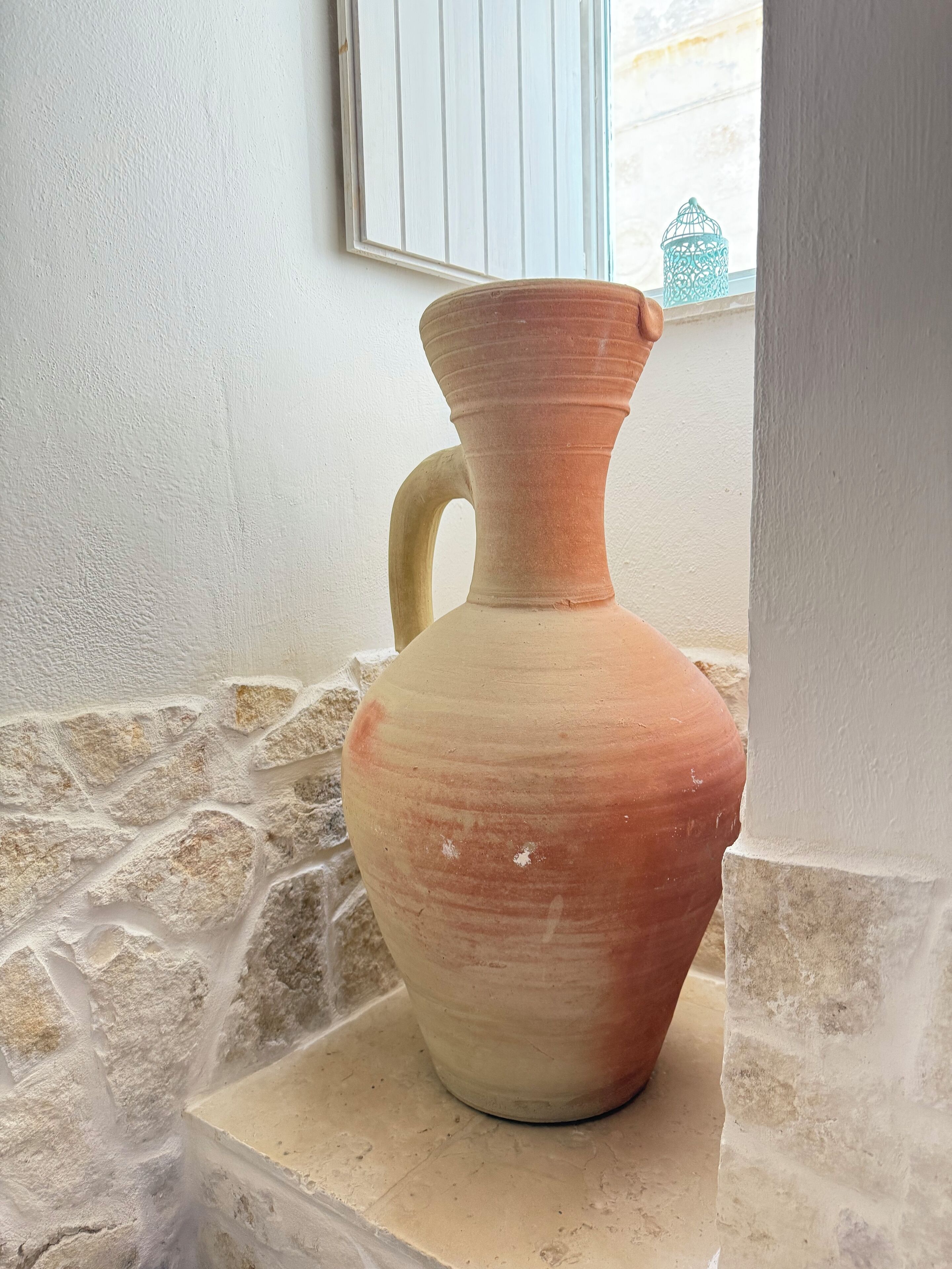 A terracotta vase with a handle on a stone ledge.