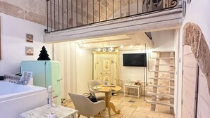 A cozy room with a stone wall, a wooden table, a chair, a small table with a candle, and a TV on the wall.