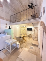 A cozy room with a stone wall, a wooden table, a chair, a small table with a candle, and a TV on the wall.
