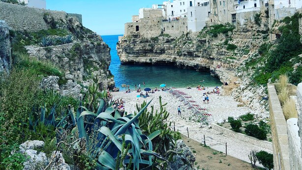 A coastal town with white buildings, a rocky beach, and clear blue skies.