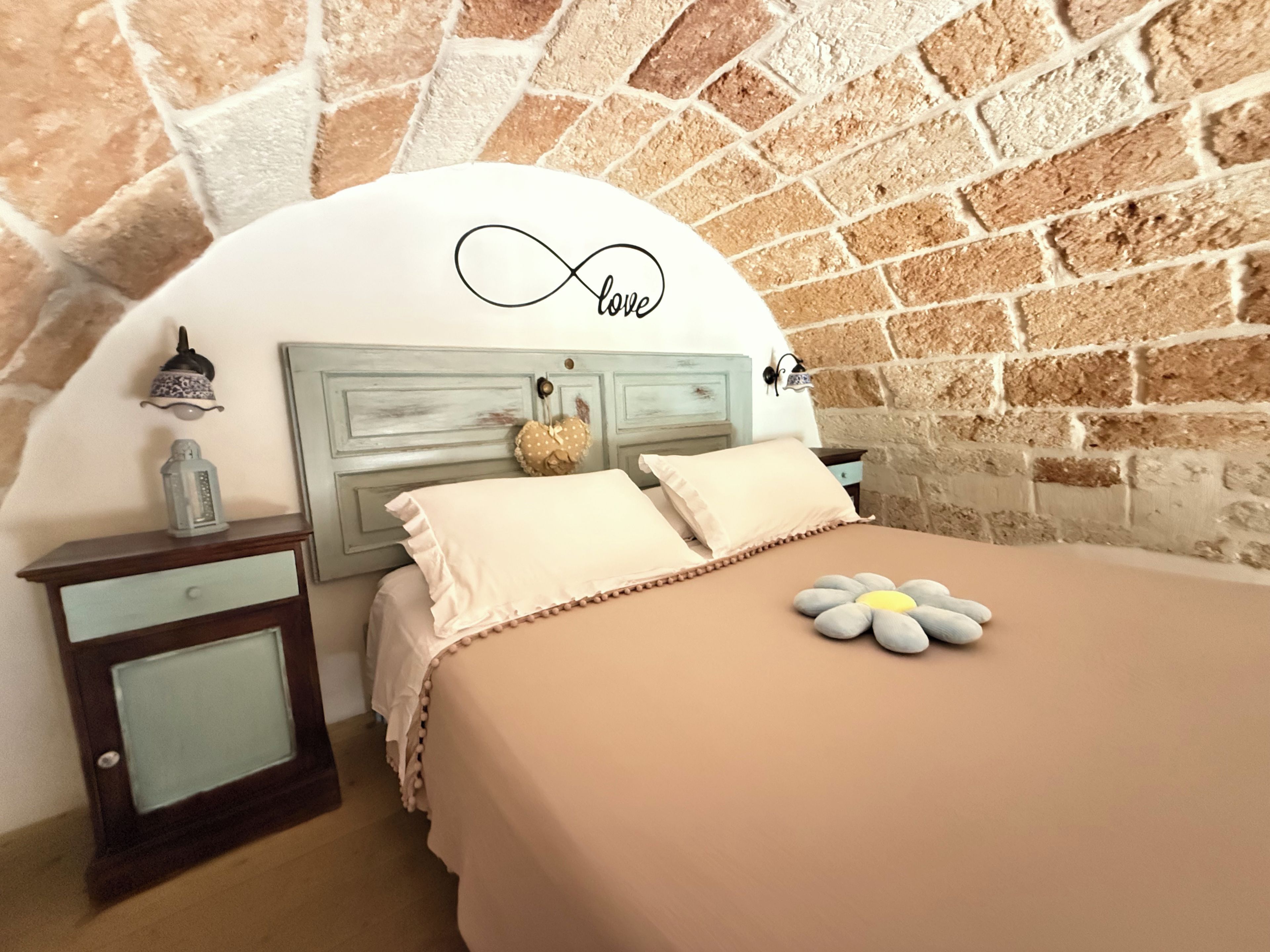 Ein Schlafzimmer mit Backsteinwand, einem Bett mit blumenförmigem Kopfkissen und einer Wandlampe.