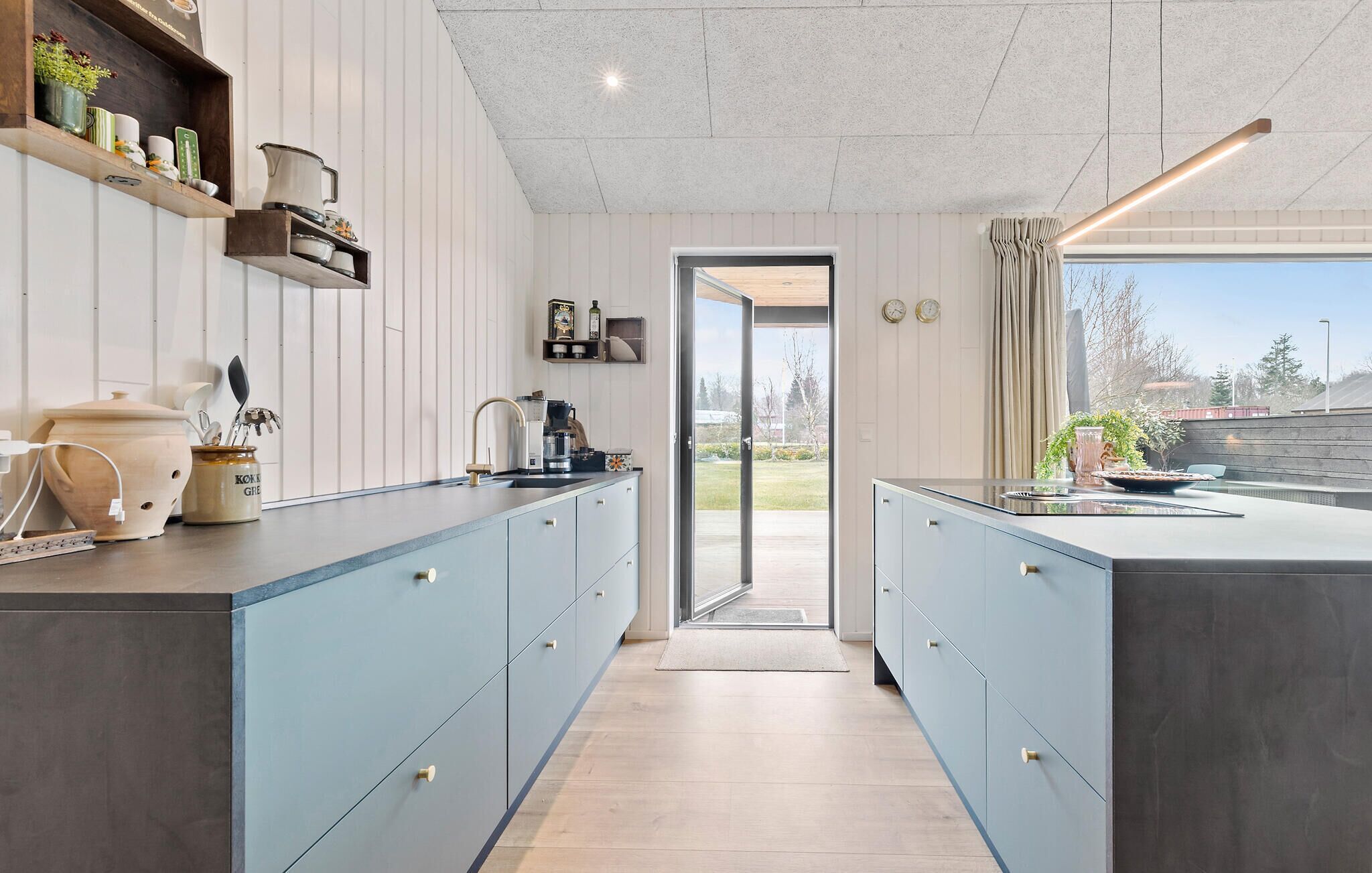 A modern kitchen with light blue cabinets, a wooden countertop, and a large window offering a view of the outdoors.