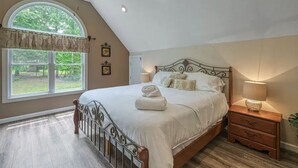 Une chambre avec un grand lit, une table de chevet, une fenêtre avec des rideaux et une vue sur la verdure.