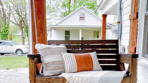 A porch with a wooden swing, a woven basket, and a house in the background.