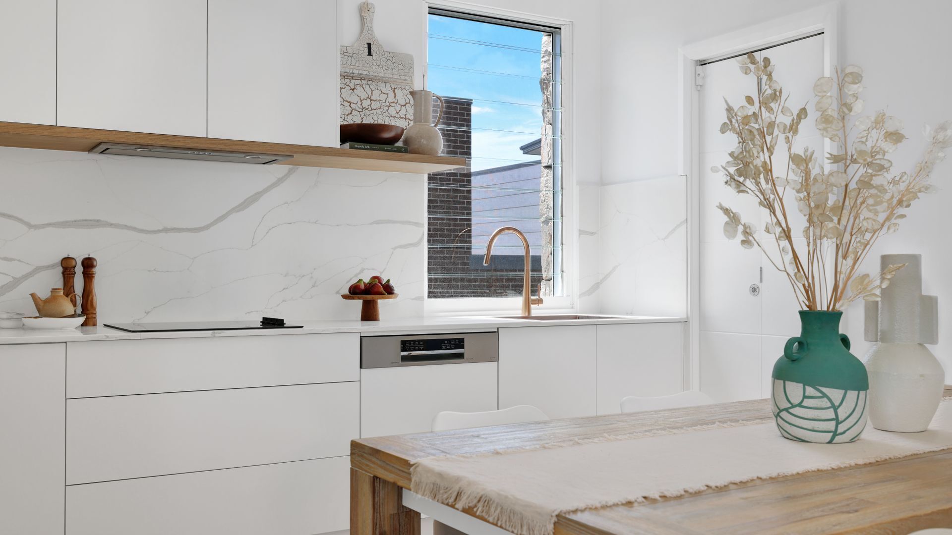 Eine moderne Küche mit weißen Schränken, einer Holz Arbeitsplatte und einem Fenster mit Blick auf ein Backsteinhaus.