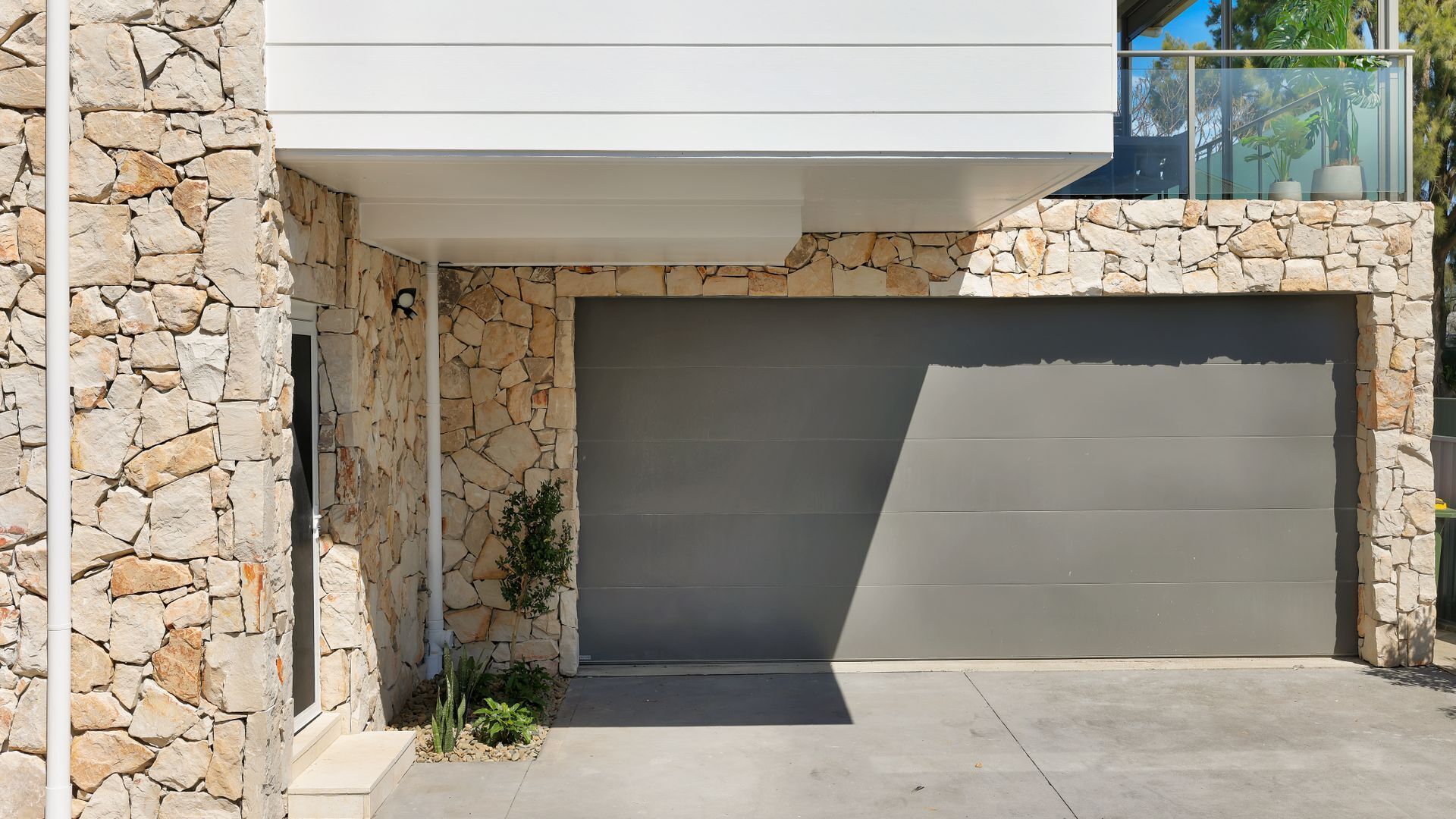 A modern house with a stone exterior, a garage door, and a small garden area with plants.