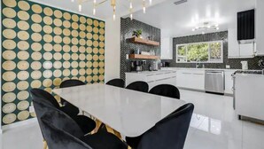 Una cocina moderna con armarios blancos, un salpicadero blanco y negro, y un comedor con una mesa blanca y sillas negras.