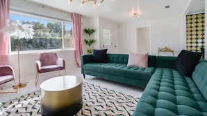 Una sala moderna con un sofá verde, sillas rosas y una alfombra estampada.