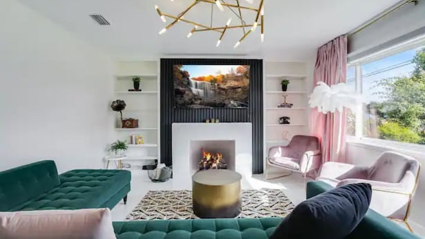 Una sala de estar moderna con chimenea, sofás verdes, una mesa de centro redonda y un ventanal con cortinas.