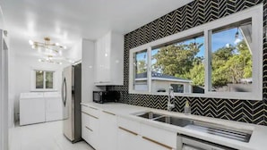 Una cocina moderna con muebles blancos, un lavavajillas Bosch y un amplio ventanal con vistas a árboles.