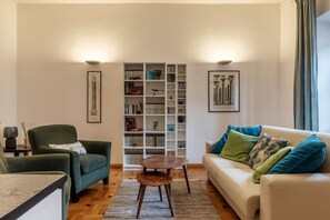 Un soggiorno con divano, poltrona, tavolino, libreria e quadri appesi alle pareti.
