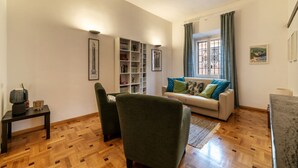 A living room with a sofa, armchairs, a coffee table, a bookshelf, and a window with curtains.