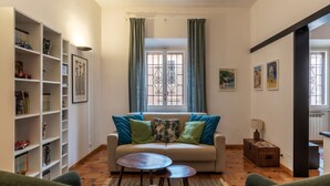 A living room with a sofa, a coffee table, a bookshelf, and a window with curtains.