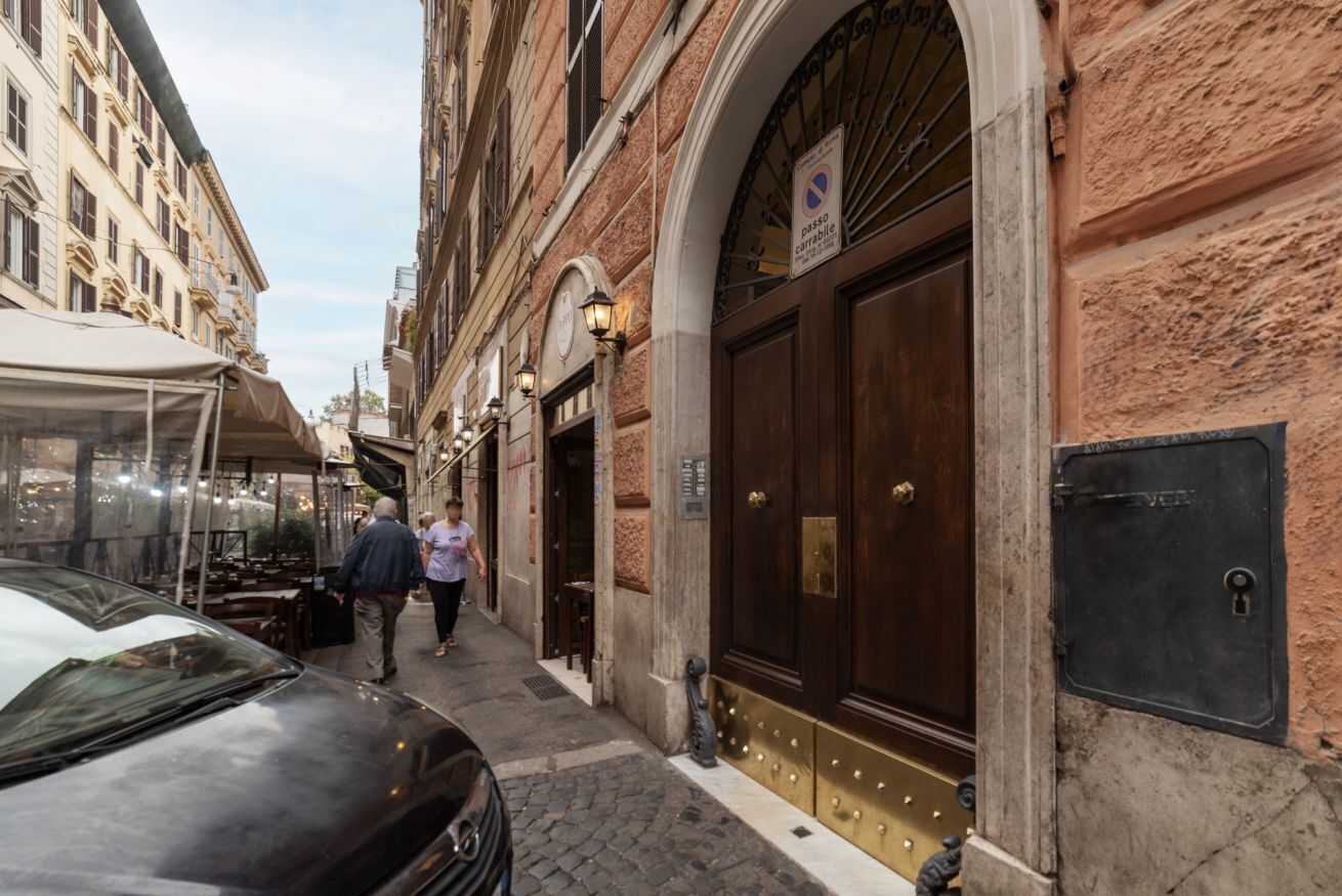 A narrow street with a building featuring a large wooden door and a sign indicating a no parking zone.