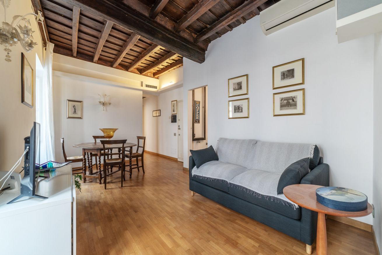 A living room with a sofa, a coffee table, a dining table with chairs, and framed pictures on the wall.