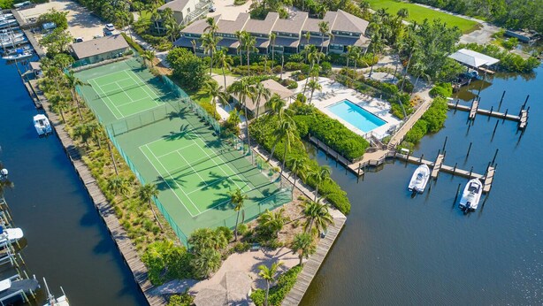 An aerial view of a resort with a tennis court, a swimming pool, and a marina with boats.