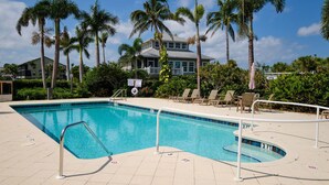 A rectangular pool with a diving board, surrounded by lounge chairs and palm trees.