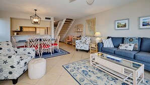 A living room with a blue sofa, patterned armchairs, a coffee table, and a staircase leading to an upper level.