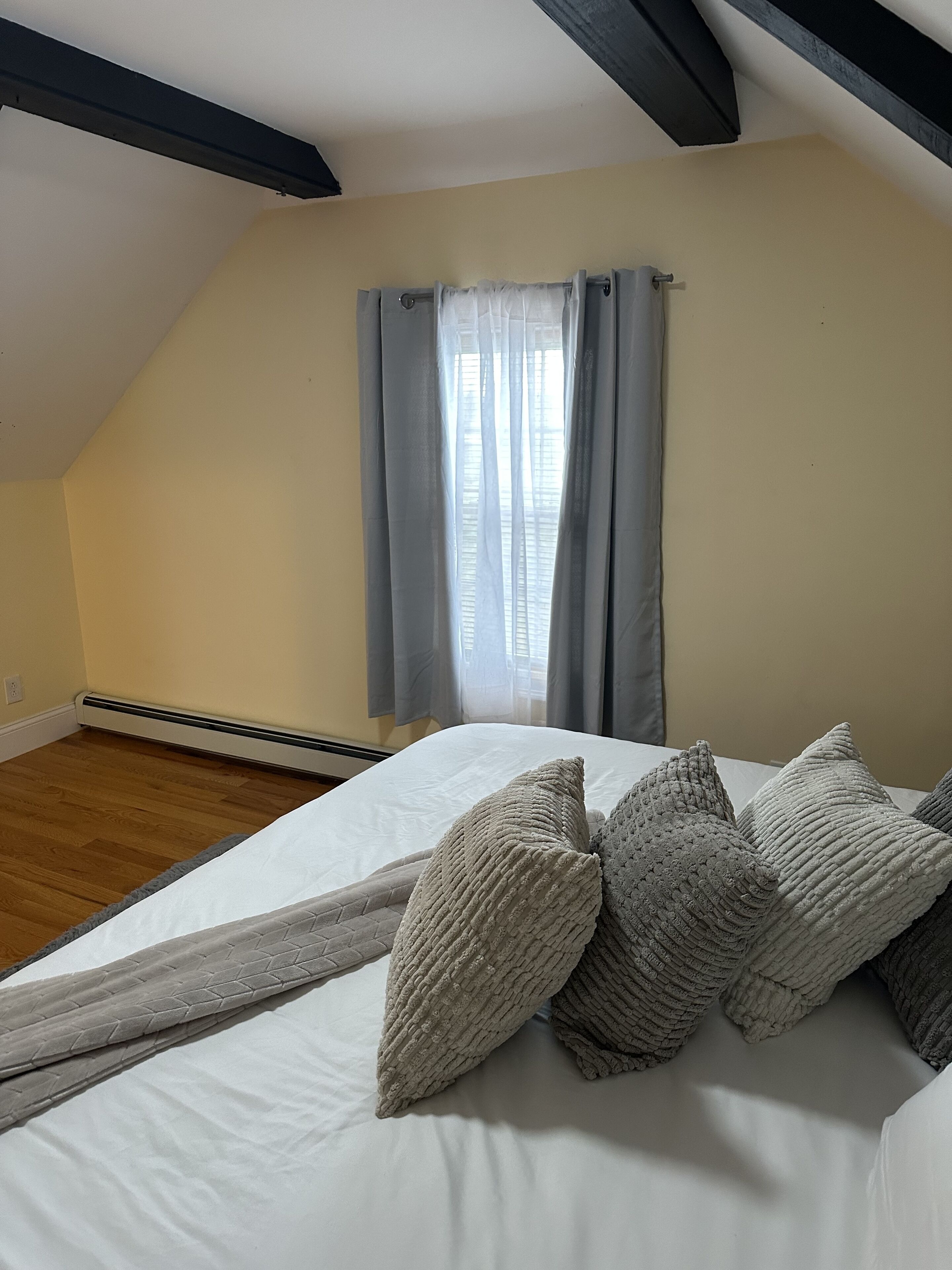 A bedroom with a sloped ceiling, a bed with multiple pillows, and a window with curtains.