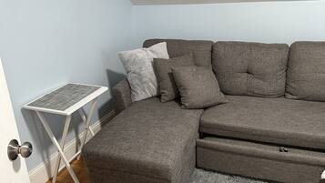 A corner room with a grey sectional sofa, a small white side table, and a grey shaggy rug.