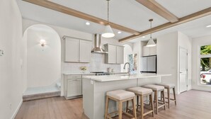 Une cuisine moderne avec des meubles blancs, un îlot central doté de tabourets et un éclairage suspendu.