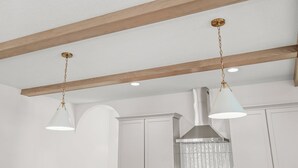 Une cuisine avec des poutres en bois, des meubles blancs et des luminaires suspendus.