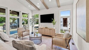 Un salon moderne doté d’un grand téléviseur, de sièges confortables et offrant une vue sur l’extérieur.