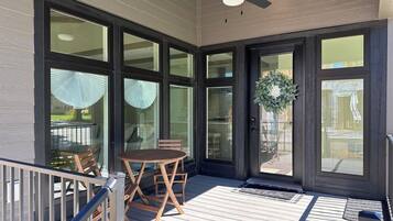 A covered outdoor area with a wooden table and chairs, large glass doors, and a ceiling fan.