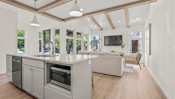 Une cuisine moderne dotée d’un îlot central, d’appareils électroménagers intégrés et de grandes fenêtres offrant une vue sur la verdure.