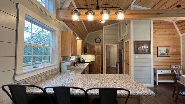 A kitchen with a granite countertop, wooden cabinets, and a built-in island with bar stools.