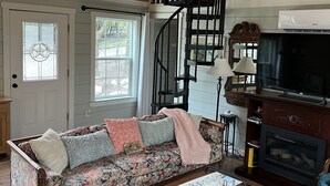 A cozy living room with a wooden ceiling, a sofa with floral upholstery, a wooden coffee table, a fireplace, and a television.