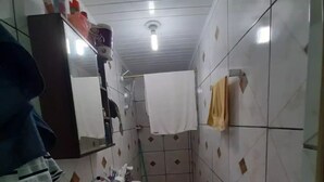 A small, narrow bathroom with white tiled walls and a white sink. There is a toilet and a mirror above the sink. - Espaço do Jonga Itacaré-ba (Itacaré)