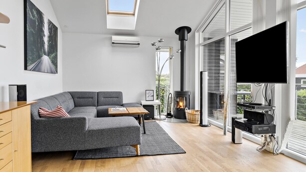 Un salon moderne avec un canapé gris, un plancher en bois, un téléviseur à écran plat, une cheminée et une grande fenêtre donnant sur un paysage verdoyant.