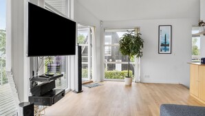 Un salon moderne avec un téléviseur à écran plat, une grande plante en pot et un tableau encadré accroché au mur.