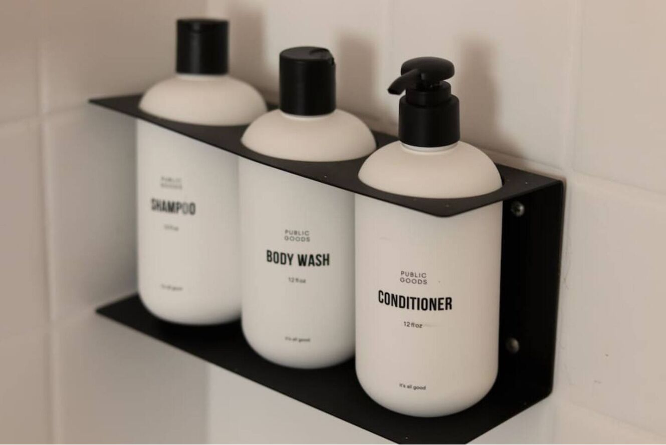 Drei weiße Flaschen mit Shampoo, Duschgel und Conditioner auf einem schwarzen Regal.