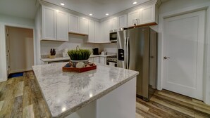 A modern kitchen with white cabinets, a marble countertop, stainless steel appliances, and a wooden floor. - Bellingham Waterfront Retreat, Private Dock, Amazing Views (Bellingham)