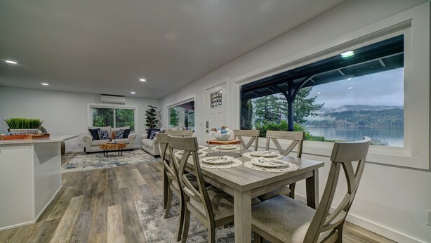 A modern dining area with a wooden table set for four, surrounded by chairs, and a view of a lake through large windows. - Bellingham Waterfront Retreat, Private Dock, Amazing Views (Bellingham)