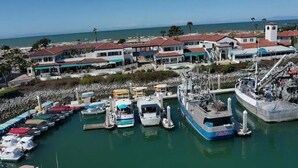 Un puerto deportivo con varios barcos amarrados, un buque grande y edificios con techos rojos al fondo.