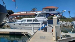 Un puerto deportivo con un yate blanco amarrado en el muelle, un edificio con tejado de tejas rojas y un cielo azul despejado.