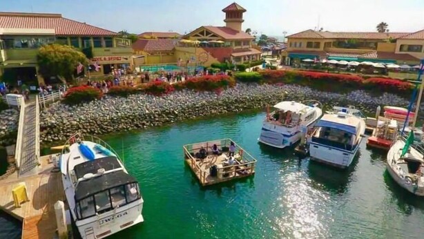 Un puerto deportivo con varias embarcaciones amarradas, un paseo marítimo y edificios con tejados de tejas rojas.